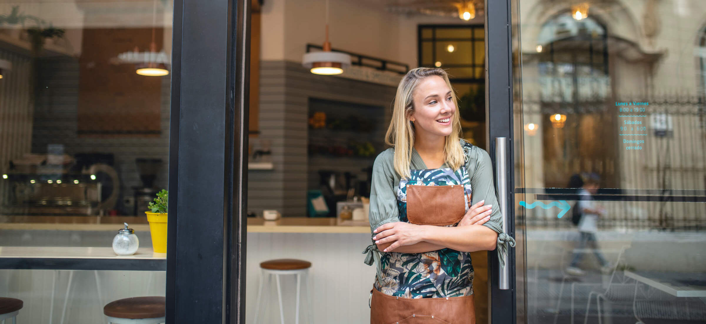 woman smiling outside hospitality business with cup of coffee